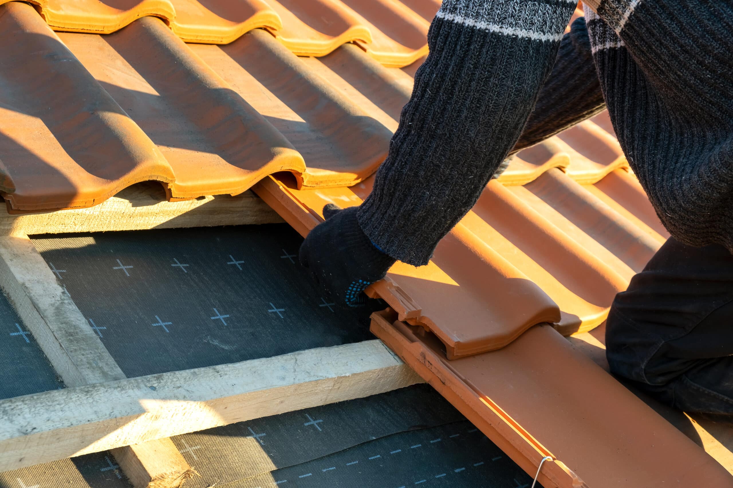 Closeup of worker hands installing yellow ceramic roofing tiles mounted